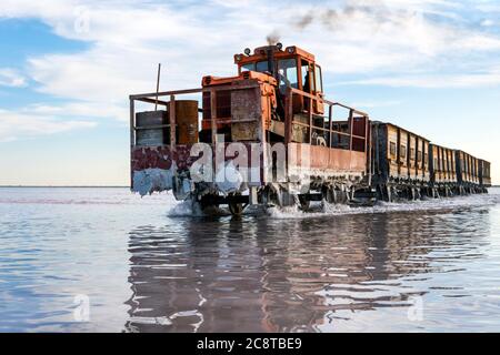 Awesome train rides on rail in the water with white salt on the background of beautiful blue sky. Stock Photo