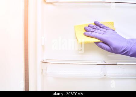 Hand in protective glove cleaning fridge. White kitchen furniture Stock Photo