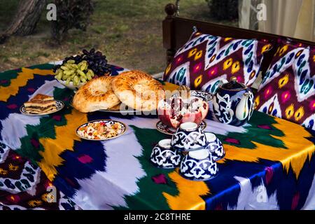 Traditional Uzbek bread on table with mugs and kettle. Cuisine of Central Asia. fruits grapes and pomegranate and sweets in plates Stock Photo