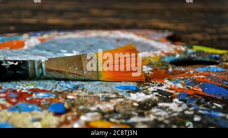 Side profile view of a paint brush resting on a paint splattered textured painting palette. Stock Photo