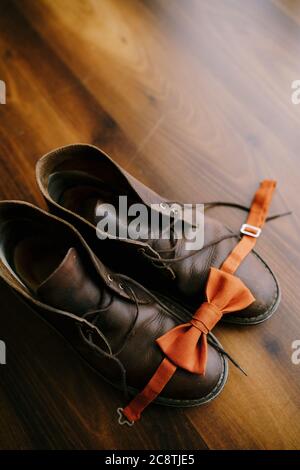 Orange bow tie for the groom on brown men's boots with untied laces. Stock Photo