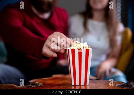 A young couple in love watching television at night romantic date night lying on the couch eating popcorn Stock Photo