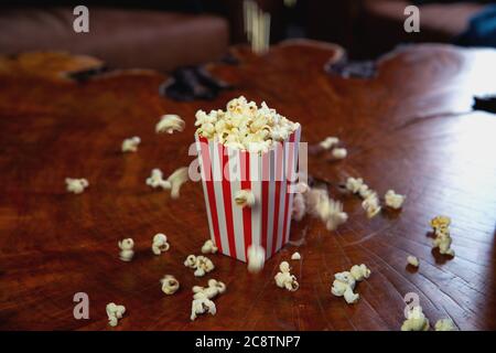 Popcorn flying out of cardboard box. red and white striped popcorn bucket with flying popcorn in the living room, movie or cinema concept Stock Photo