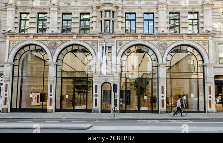 London, UK - April 24, 2020: A man walking with a bicycle past the landmark Apple Store on London's Regent Street where almost all shops have been clo Stock Photo