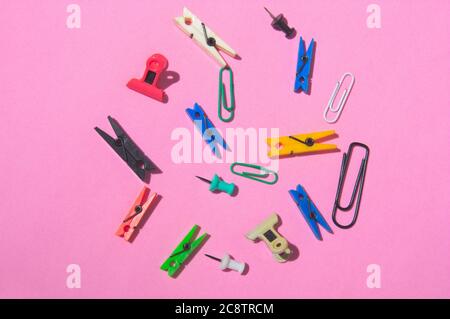 Close-up of a set forming an irregular circle with office supplies such as clips, tweezers, thumbtacks scattered on a pink surface with direct side li Stock Photo
