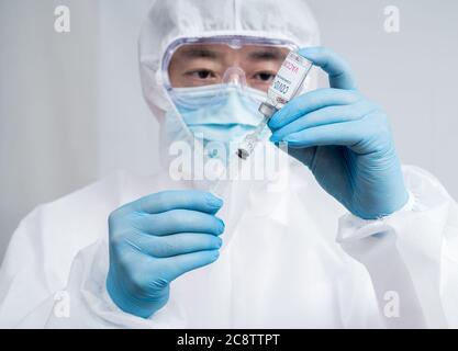 A male scientist wearing blue gloves and a protective suit holding a Covid-19 vaccine. Stock Photo