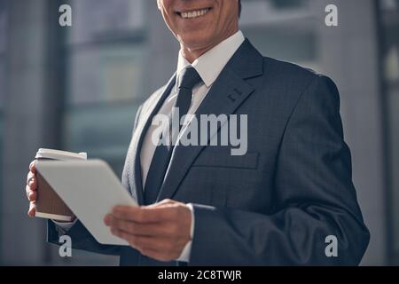 Cheerful man with cup of coffee using tablet computer outdoors Stock Photo