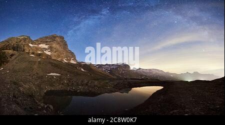 Panoramic view scenery of mountain peak Matterhorn at night under Milky way with shining stars in dark sky. Beautiful mountains area in Alps with high rocky peaks and lake with clear water. Stock Photo