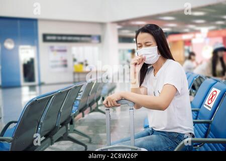 Asian tourist feeling sick, coughing ,wearing mask and sit on chair with social distancing to prevent pandemic during travel at airport terminal.