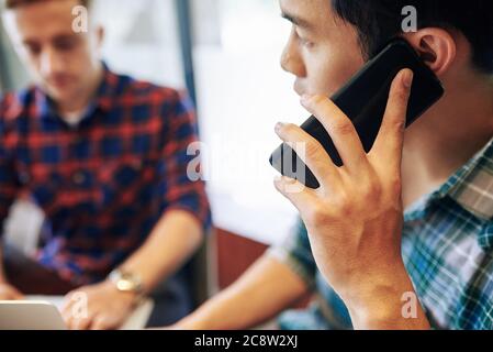 Young Asian businessman talking on phone when his colleague working on laptop Stock Photo