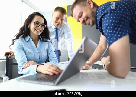 Business partners in office are smiling and watching presentation on laptop Stock Photo