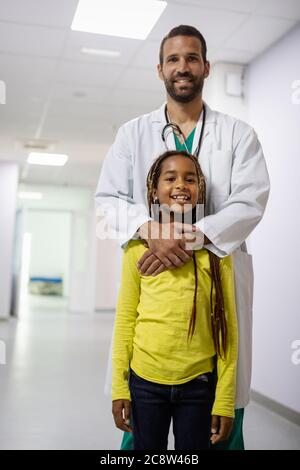 Pediatrician doctor smiling with his little girl patient at hospital Stock Photo