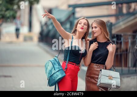 two cheerful modern female tourists while sight seeing in old town. one woman points up to a sight. other excited woman look up, too. Stock Photo