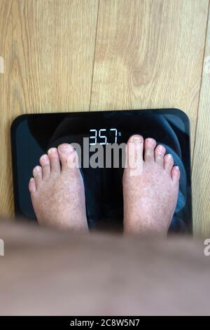 Obese mans point of view looking at his feet and BMI on the weighing scales Stock Photo