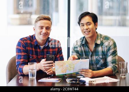 Portrait of joyful multi-ethnic friends sitting at cafe table and discussing map of the city they are going to travel to Stock Photo