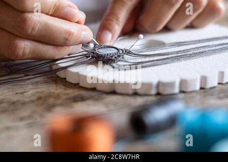 Detailed macro close-up of woman fingers working on a handmade knotted micro macrame bracelet with blurred spools of thread in bokeh effect - Working Stock Photo