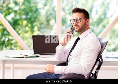 Shot of thinking businessman sitting at office desk and talking with somebody on his cell phone. Stock Photo