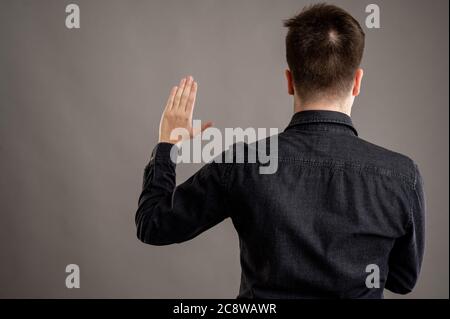 Back view of serious stylish attractive man dressed with a casual black shirt taking oath isolated on grey background with copy space advertising area Stock Photo