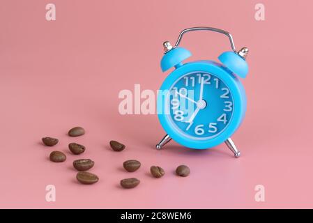 Blue alarm clock and coffee beans on pink background. Time to wake up and drink coffee. Good morning and start of new day concept Stock Photo