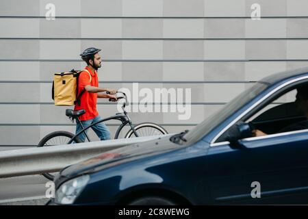 Delivery by courier in city. Guy in helmet and with backpack, going through city with bicycle