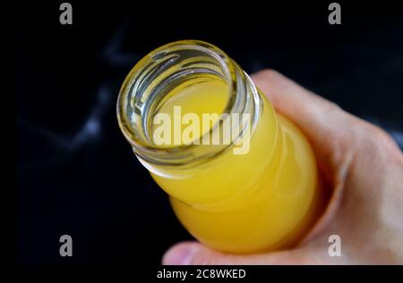 Closeup an opened bottle of orange juice in hand on black background Stock Photo