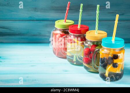 Assorted detox water cocktails in glass jars on wooden background, fresh berries and fruits mix Stock Photo