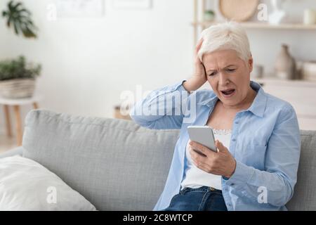 Mobile Scams Concept. Shocked Senior Woman Looking At Smartphone Screen In Frustration Stock Photo