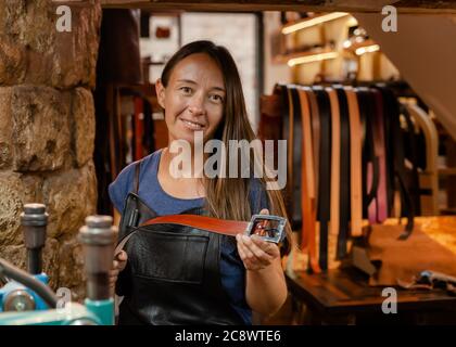 Young leather craftswoman in her traditional workshop holding a handmade belt Stock Photo