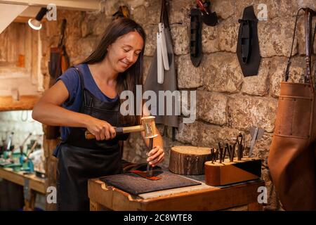 Leather craftswoman in her atmospheric workshop working on a hand-made belt. concept: female artisan lifestyle Stock Photo