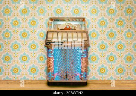 Colorful vintage jukebox in front of retro flower wallpaper on a wooden floor Stock Photo