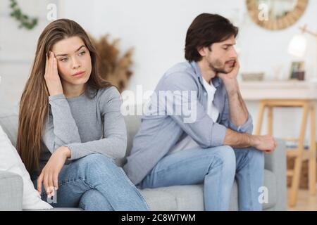 Upset young couple sitting on sofa at home, having conflict Stock Photo