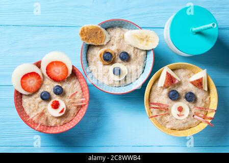 Funny bowls with oat porridge with cat, dog and mouse faces made of fruits and berries, food for kids idea, top view Stock Photo