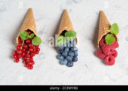 Fresh berries in waffle cones on stone background, raspberry, blueberry and redcurrant with mint leaves Stock Photo
