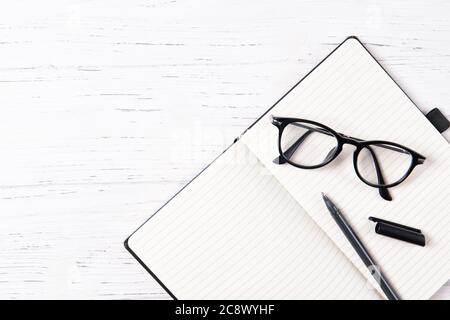 Office desk with empty notepad, pen and glasses, wooden background, top view with copy space Stock Photo