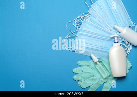 Stack of Disposable blue medical face masks, rubber latex gloves and alcohol hand sanitizer antiseptic on blue background Stock Photo