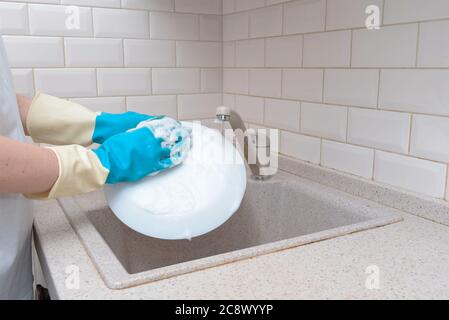Woman washes dishes. Washing dishes - hands with gloves in kitchen, housework Stock Photo