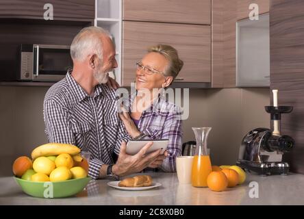 Elderly retired couple watching a video together on a tablet in a kitchen Stock Photo