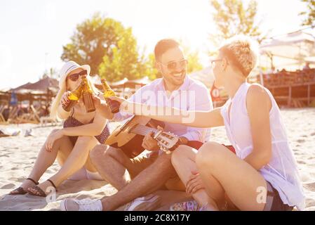 Closeup of three caucasian friends sitting on the beach and drinking beer Stock Photo