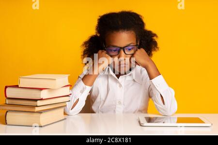 Sad African Schoolgirl Sitting At Digital Tablet Bored, Yellow Background Stock Photo