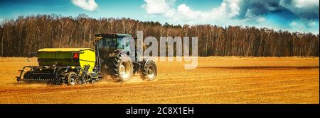 farmer with tractor seeding - sowing crops on agricultural field in spring. banner copy space Stock Photo