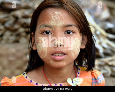 Young Burmese girl with natural thanaka face cosmetic all over her face gapes at the camera. Stock Photo