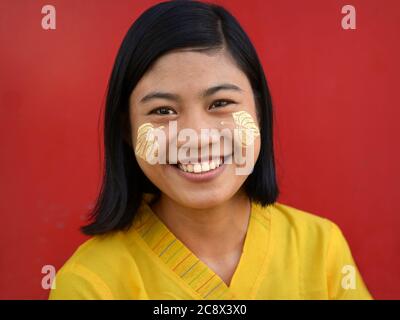 Young Burmese woman with leaf-shaped traditional thanaka face cosmetic on her cheeks smiles for the camera. Stock Photo