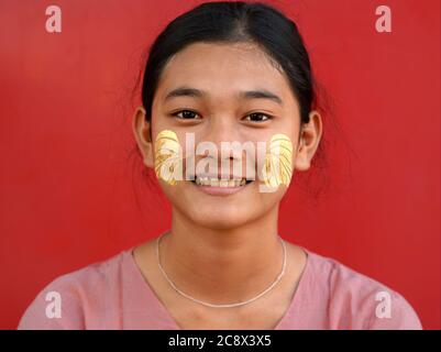 Young Burmese woman with leaf-shaped traditional thanaka face cosmetic on her cheeks smiles for the camera. Stock Photo