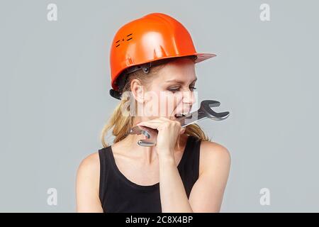 blonde girl. in a protective helmet holds a large wrench in his hands. photo session in the studio on a white background Stock Photo
