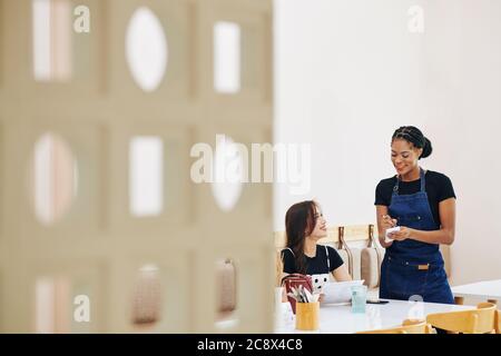 Pretty smiling Black cafe waitress writing down order of cheerful female customer Stock Photo