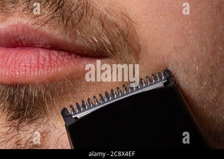 A man shaves his beard with a trimmer razor. Modeling beard, masculine style, facial hair care, morning routines in the bathroom. Close up. Stock Photo