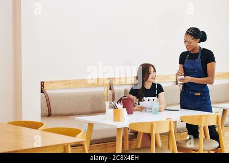 Positive waitress talking to female customer and writing down her order Stock Photo