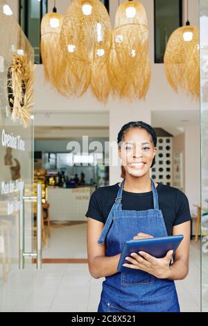Happy smiling pretty waitress using application on tablet computer when working in cafe Stock Photo