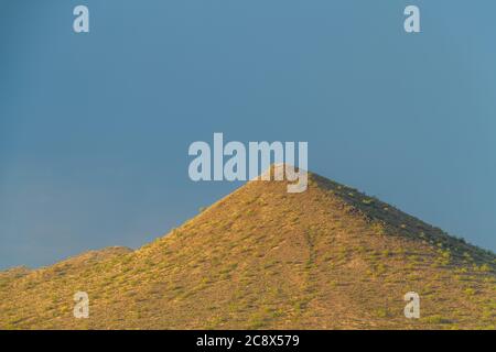 A desert mountain lit by the morning sun with dark, ominous clouds in the background. Stock Photo