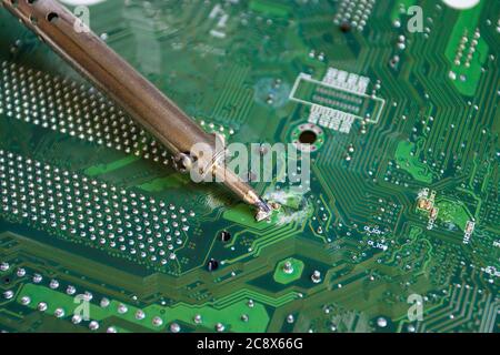 soldering iron on green mainboard for repairing electronic of the computer circuit board concept technology of computer circuit hardware Stock Photo
